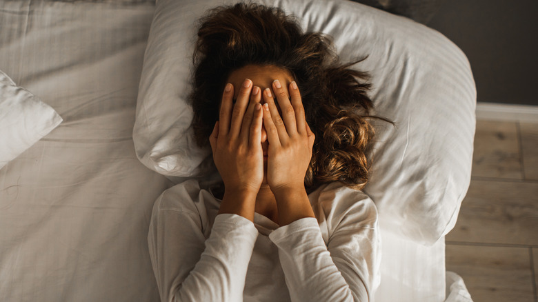 A woman in bed with her hands covering her face